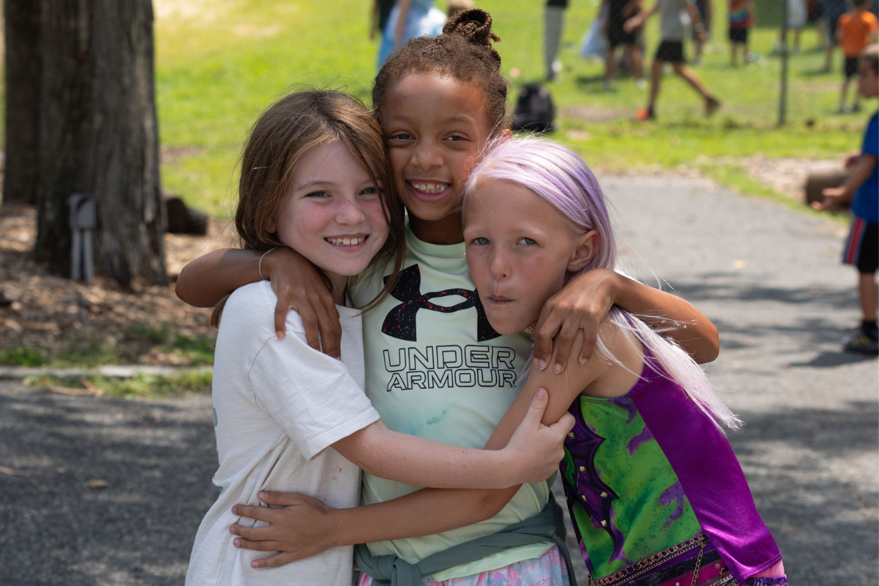 Untitled design (54) Group of children and a camp counselor posing together outdoors at a summer camp,